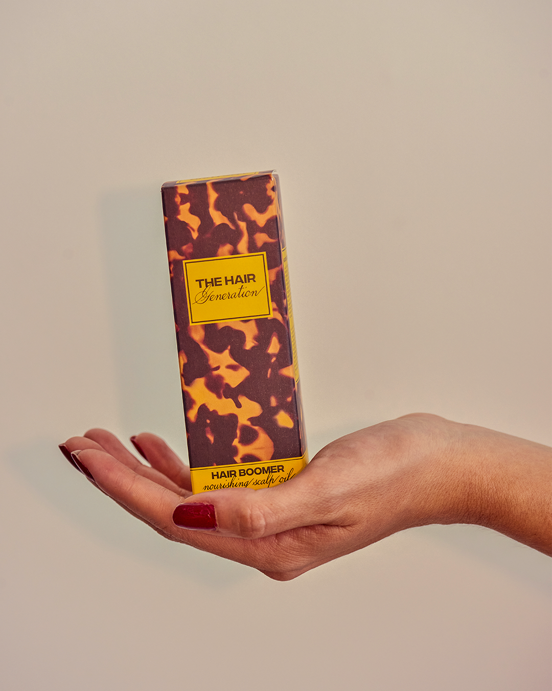 Hand holding a box of 'The Hair Groomer' with a camouflage design on a beige background