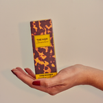Hand holding a box of 'The Hair Groomer' with a camouflage design on a beige background