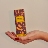 Hand holding a box of 'The Hair Groomer' with a camouflage design on a beige background